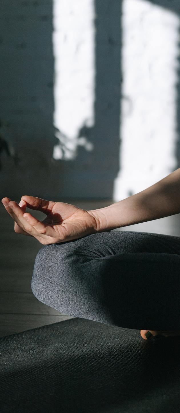 Main de Margaux posée sur le genou, doigts en geste de méditation, sur un tapis de yoga